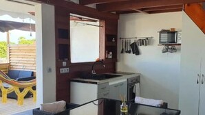 Een kleine keuken met een gootsteen, fornuis en magnetron, een glazen tafel en een rieten stoel.