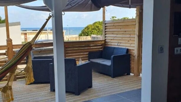 Een overdekt terras met een hangmat, een bank en uitzicht op zee.