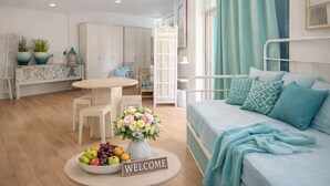 Ein modernes Schlafzimmer mit Bett, Nachttisch mit Willkommensschild, Essbereich mit Tisch und Stühlen sowie Küchenzeile mit Schränken und Kühlschrank.