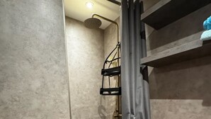 Ein kleines, modernes Badezimmer mit Dusche, einem Holzregal und einem Handtuchhalter.