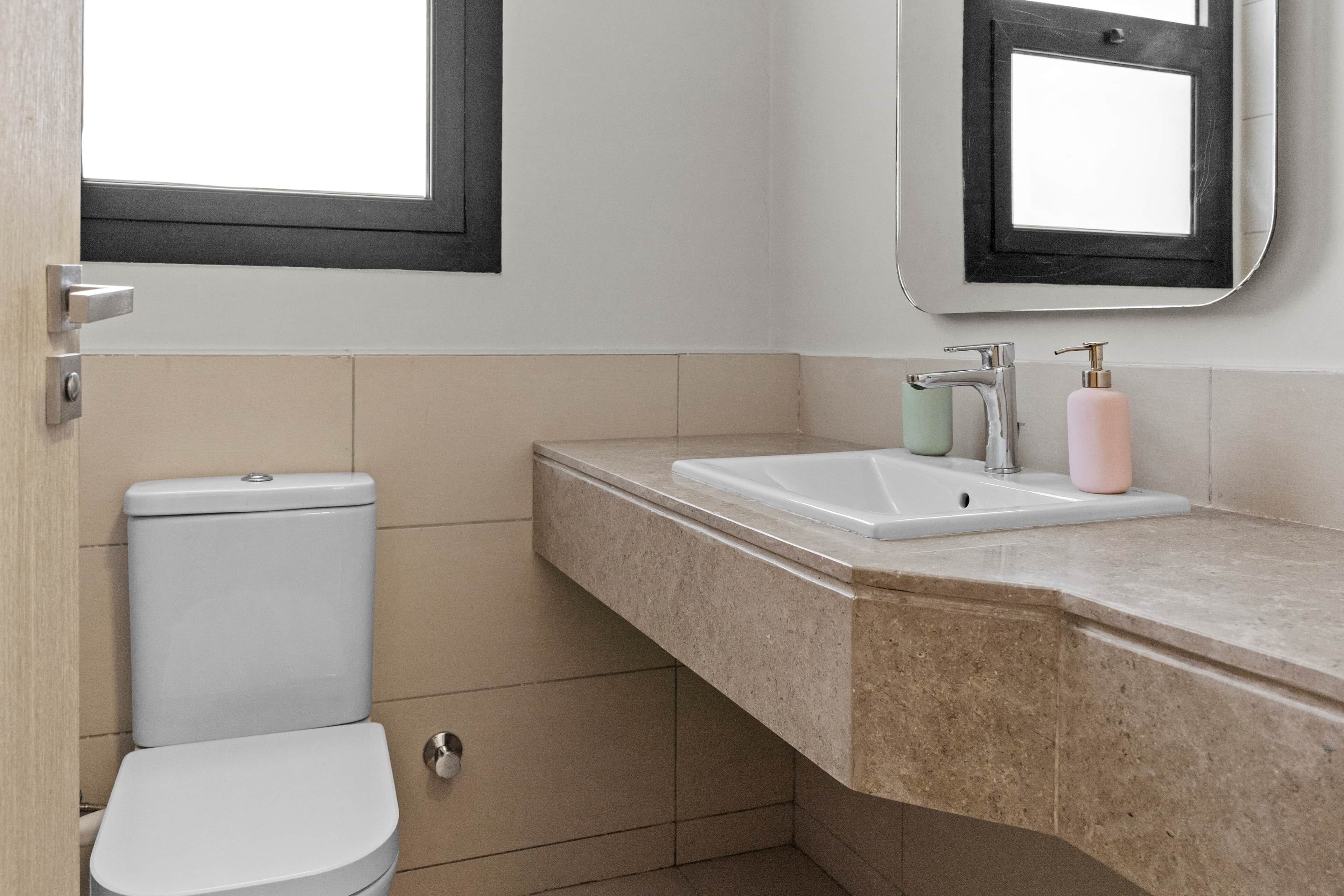 A bathroom with a toilet, sink, and mirror.