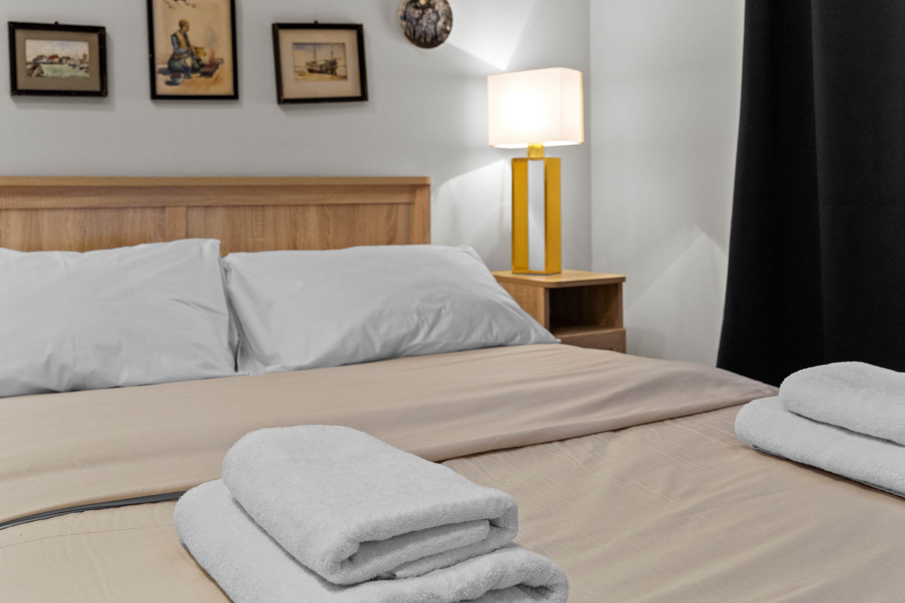 Un lit bien fait, avec des draps blancs, une tête de lit en bois et une lampe de chevet.