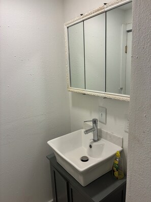 A bathroom with a white sink, a mirror with a decorative frame, and a bottle of hand soap on the counter.