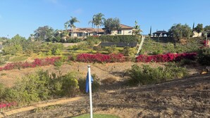 A golf course with a flagstick in the center of a green, surrounded by dry grass and bushes. - Luxury Wine Country Casita with Extraordinary Ridgetop Views Extensive Amenities (Fallbrook)