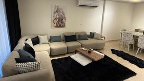 A modern living room with a sectional sofa, a coffee table, and a dining area with a table and chairs. - 3-bedroom apartment in gorgeous SHIKH ZAYED with AC and comfort (giza)