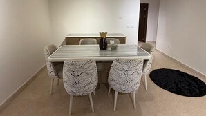 A modern dining area with a glass-top table, four patterned chairs, a vase, and a black rug. - 3-bedroom apartment in gorgeous SHIKH ZAYED with AC and comfort (giza)