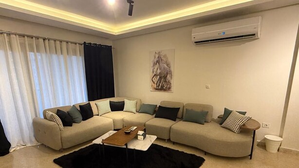 A modern living room with a beige sectional sofa, a black furry rug, and a wooden coffee table. - 3-bedroom apartment in gorgeous SHIKH ZAYED with AC and comfort (giza)