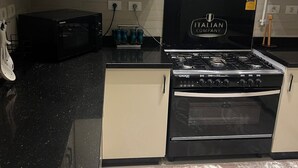 A modern kitchen with white cabinets, a black stove, and a microwave. - 3-bedroom apartment in gorgeous SHIKH ZAYED with AC and comfort (giza)