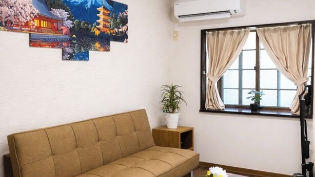Ein Wohnzimmer mit einer Couch, einem Couchtisch, einer Zimmerpflanze und einem Fenster mit Vorhängen.