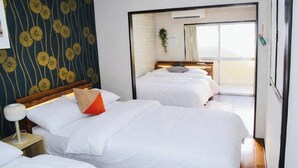 Ein Hotelzimmer mit zwei Betten, einem Nachttisch, einer Lampe, einem Fenster mit Vorhängen und einer Wand mit floralem Muster.