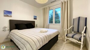 A bedroom with a bed, a chair, a window with curtains, and a wall-mounted lamp. - Villa Ostrea - ANDERNOS LES BAINS (ANDERNOS LES BAINS)