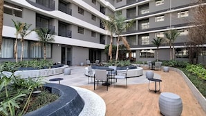 Une cour extérieure moderne, aménagée avec des espaces de détente, des palmiers et un immeuble à plusieurs étages doté de balcons.