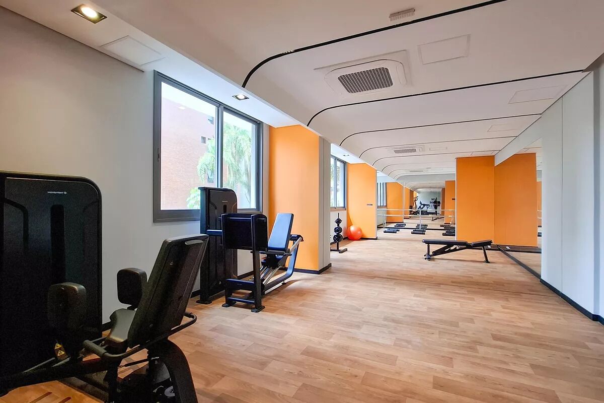 Ein Fitnessraum mit Trainingsgeräten, großen Fenstern und orangen Wänden.