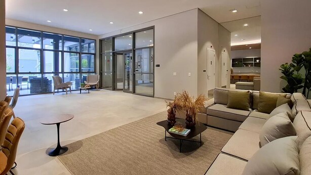 Un salon moderne comprenant un canapé, des fauteuils, une table basse et une petite table. De grandes fenêtres et une porte vitrée donnent accès à une autre pièce.