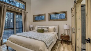 Una camera da letto con un letto grande, due comodini con lampade e due finestre vista alberi.