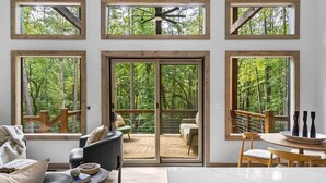 Un'ampia zona giorno con grandi finestre che offrono vista sul bosco, un balcone con posti a sedere all'aperto e un arredamento moderno.