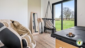 A modern room with a massage table, a hanging chair, and a large window offering a view of the outdoors.