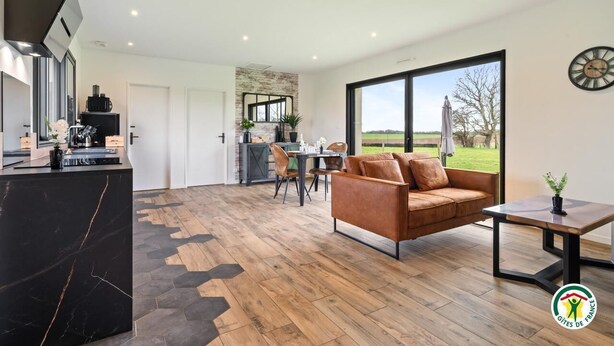 A spacious living area with a large window, a black marble coffee table, a brown leather sofa, and a dining area with a table and chairs.