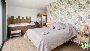 A bedroom with a bed, a bench, a desk, and a shower area.