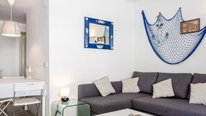 A modern living room with a grey sofa, a glass coffee table, and a white desk with a chair. A hammock is hung on the wall, and a framed picture is displayed above the sofa. - Apartament Antic Plankton - Sa Riera Begur - Free Parking, Beach, Wifi, holidays (Sa Riera)