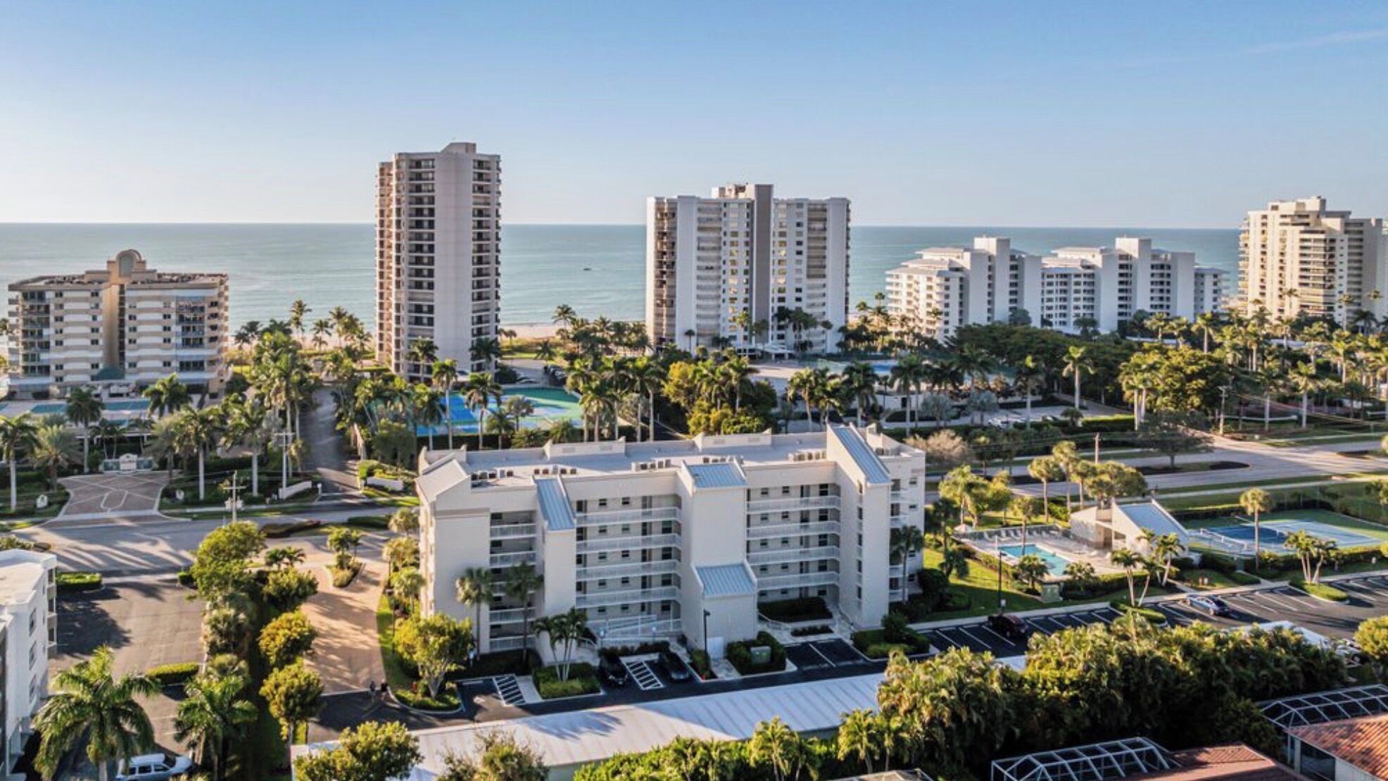 Un resort con varios edificios altos, un estacionamiento central y vista a la playa.