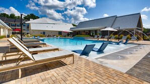 A swimming pool with lounge chairs, a covered seating area, and a building with a sloped roof. - Charming 3-bedroom Villa with garage in Madison-sleeps 10 (Madison)