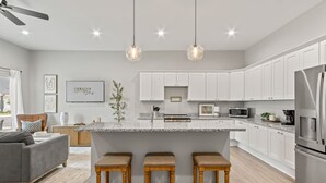 A modern kitchen with white cabinets, a central island with stools, and stainless steel appliances. - Charming 3-bedroom Villa with garage in Madison-sleeps 10 (Madison)