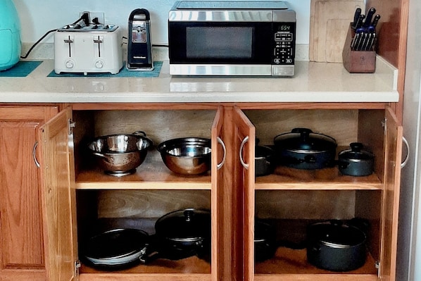 A kitchen with a microwave, toaster, and various pots and pans on shelves.