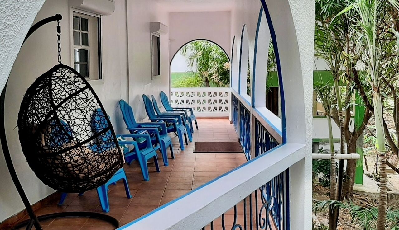 Un espace extérieur abrité, aménagé avec des chaises en plastique bleues et un fauteuil suspendu.
