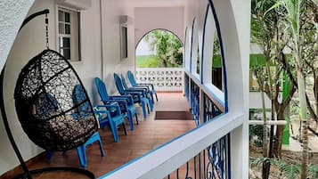 Un espace extérieur abrité, aménagé avec des chaises en plastique bleues et un fauteuil suspendu.