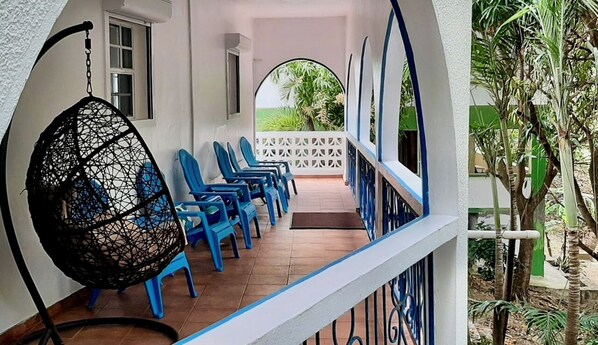 A covered outdoor seating area with blue plastic chairs and a hanging chair.
