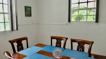 Une table à manger avec une horloge, entourée de chaises en bois, dans une pièce dotée de fenêtres et ornée d’un petit tableau au mur.