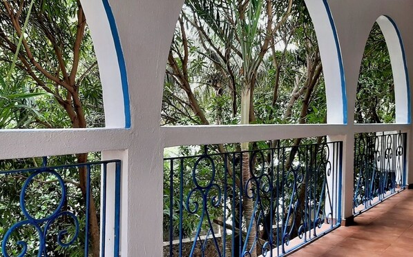 Un balcón techado con vistas a árboles y suelo de baldosas.