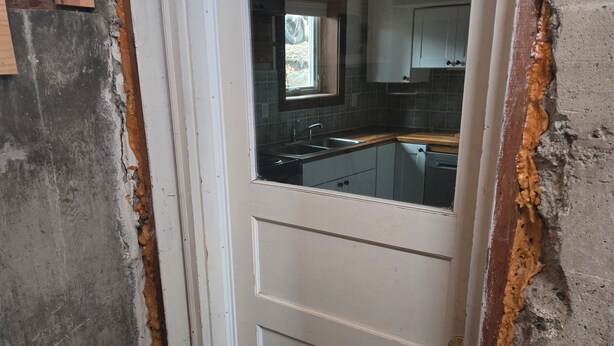 A door with a window, a kitchen visible through the window, and a damaged wall. - Cute Southside Private Apartment in Bozeman (Bozeman)