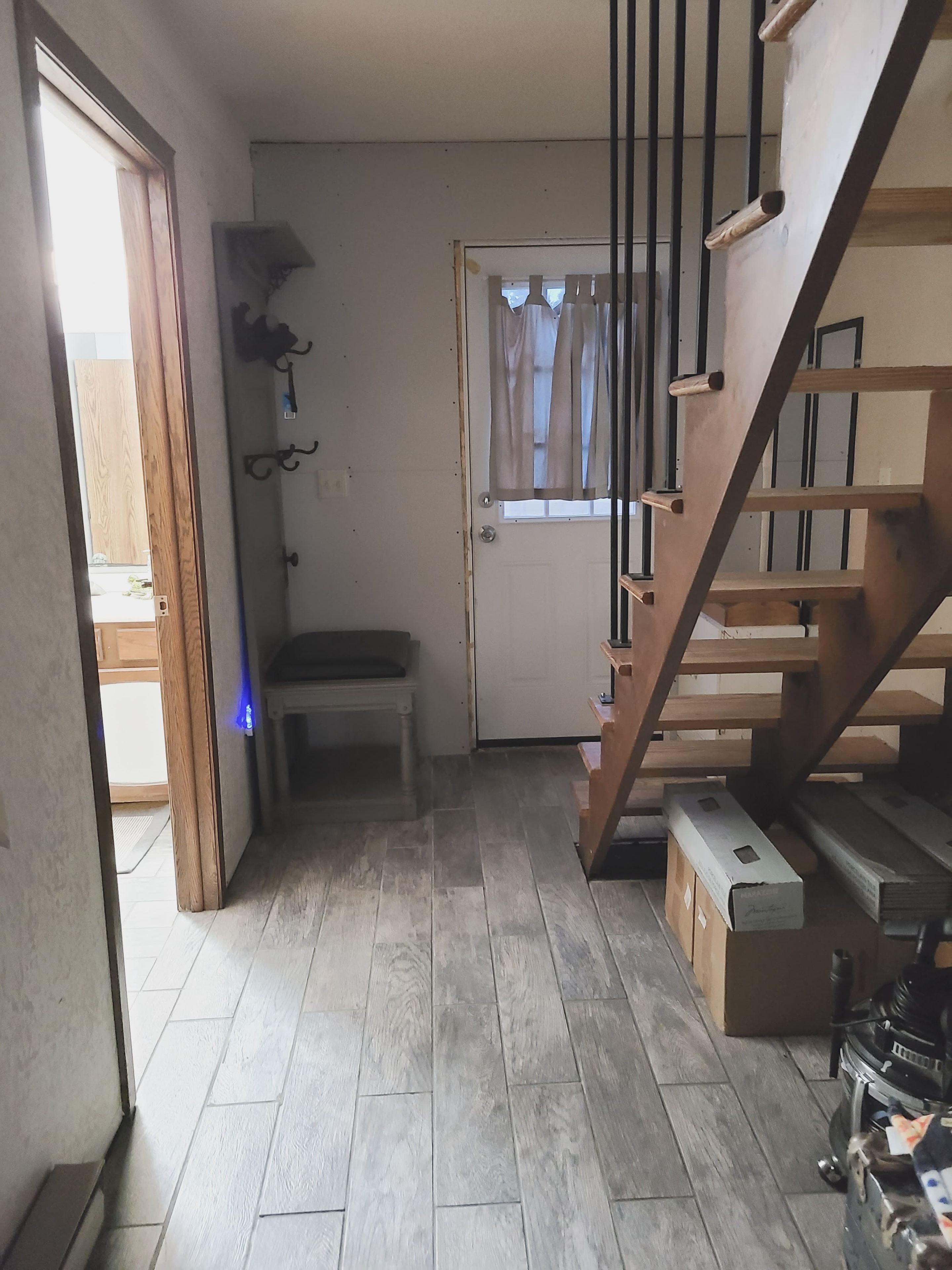 A hallway with a wooden staircase, a bench, and a door with a window.