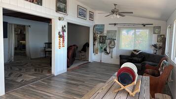 A spacious living area with a wooden floor, a ceiling fan, and a dining table with a red bowl.