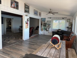 A spacious living area with a wooden floor, a ceiling fan, and a dining table with a red bowl.