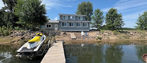 Une propriété au bord du lac, dotée d’un quai, d’un jet ski et d’une maison avec de nombreuses fenêtres.