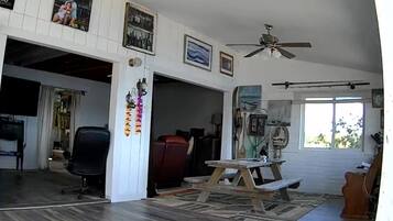 Un vaste espace de vie agrémenté d’un ventilateur de plafond, d’une table en bois et d’une grande fenêtre laissant entrer la lumière naturelle.