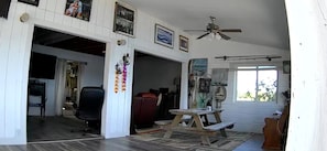 A spacious living area with a ceiling fan, a wooden table, and a large window providing natural light.
