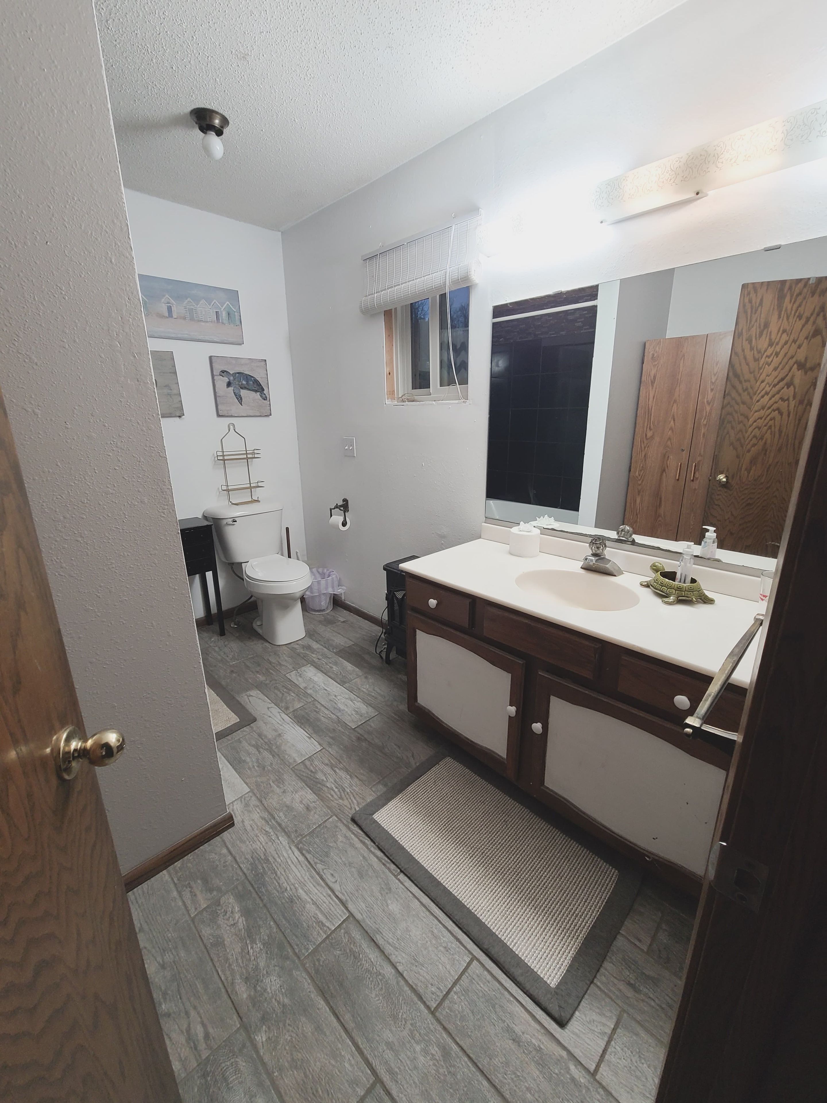A bathroom with a wooden vanity, a white sink, a mirror, and a window.