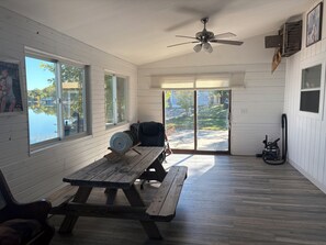 A room with a wooden table, a ceiling fan, and a view of a lake through large windows.