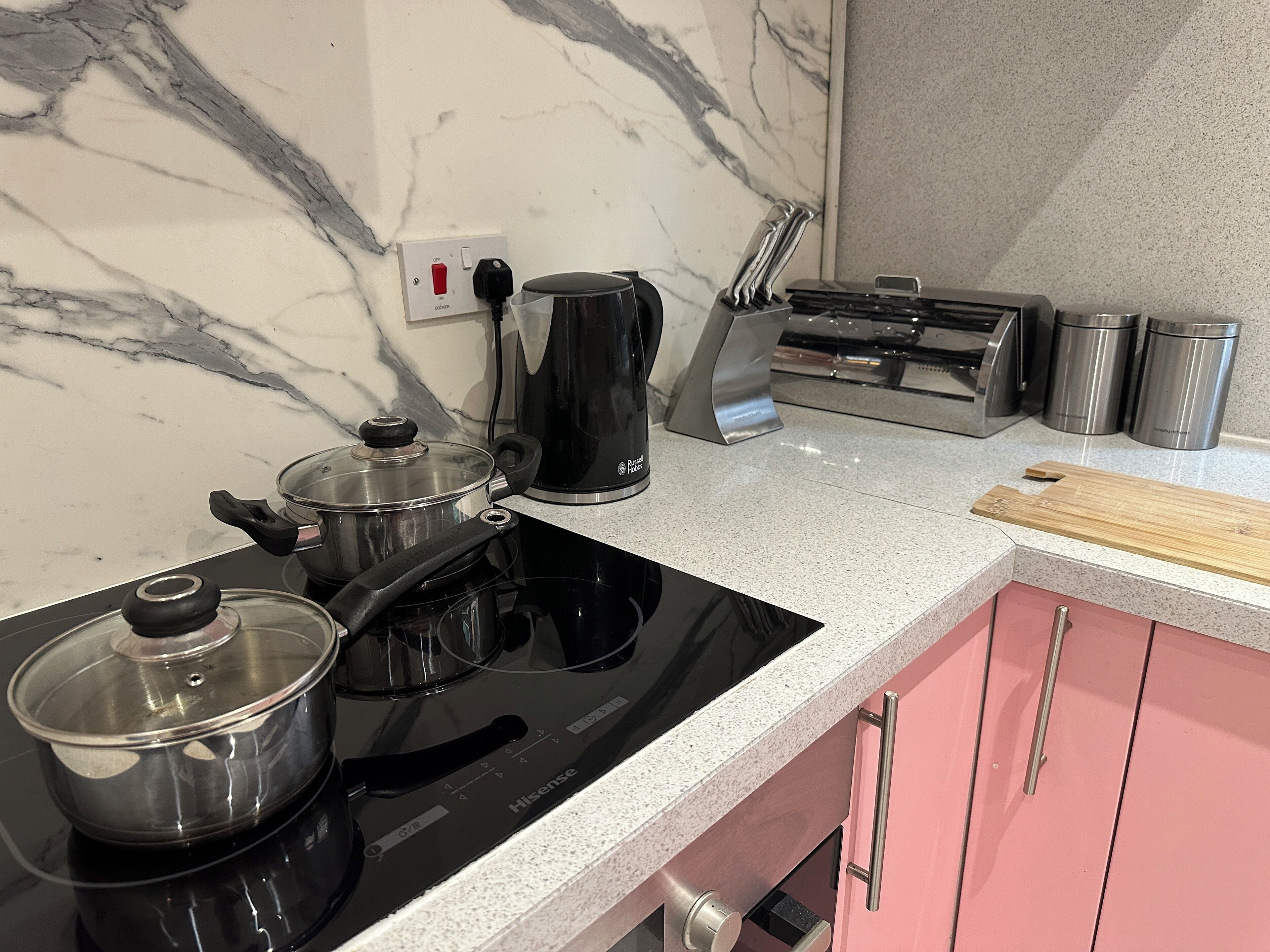 Une cuisine équipée d’une plaque de cuisson à induction noire, d’une casserole, d’une bouilloire, d’un grille-pain et de récipients en acier inoxydable.