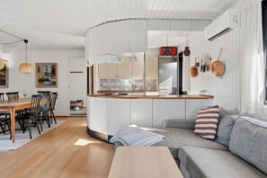 A modern kitchen with white cabinetry, a wooden dining table, and a gray sofa. - Holiday home for 2 families by the water (Væggerløse)