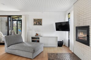 Ein Wohnzimmer mit einer Couch, einem Kamin, einem Wand-Fernseher und einem Bücherregal.