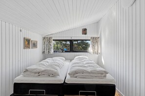 Ein Zimmer mit zwei Betten, einem Fenster mit Vorhängen und einem kleinen Bild an der Wand.