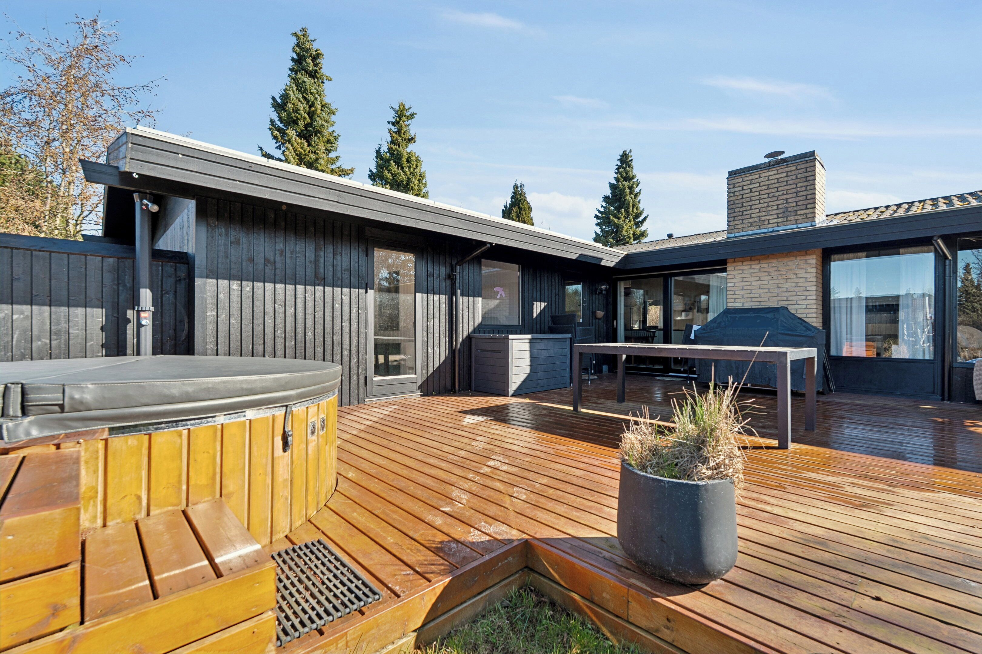 A modern outdoor deck with a hot tub, barbecue area, and a potted plant.