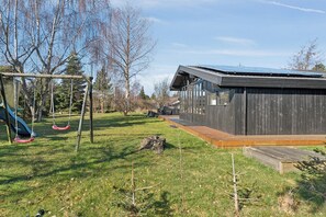 Ein modernes Gebäude mit einer Holzterrasse, einer Schaukel und einem Rasen.
