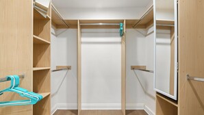 Ein begehbarer Kleiderschrank mit Holzböden, einer zentralen Kleiderstange und einem türkis bunten Kleiderbügel links.