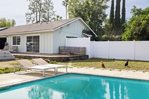 Un jardin avec une piscine, une maison blanche, un patio couvert et une clôture blanche.